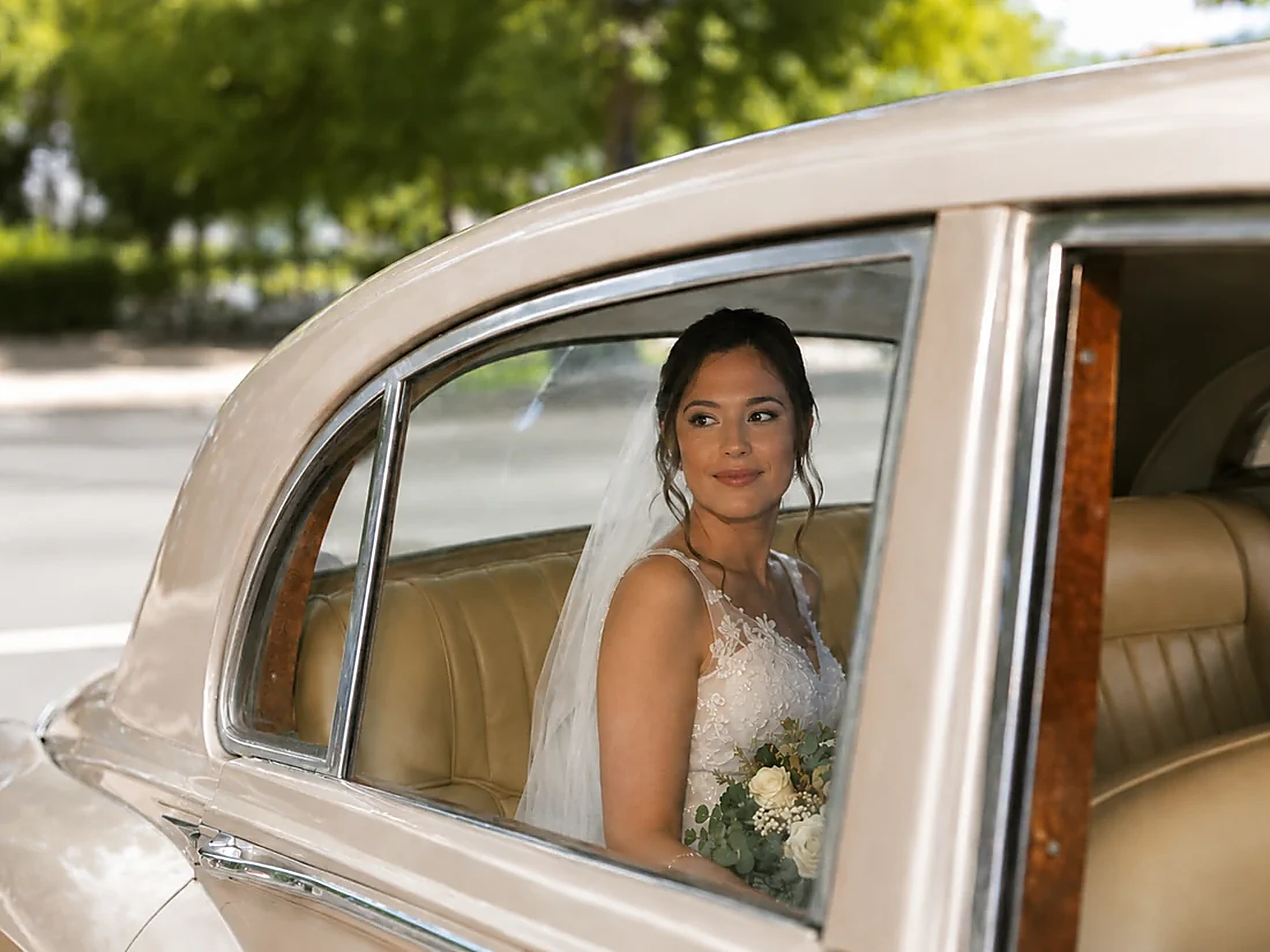 A bride in her veil seated in the back of the 1950s Rolls-Royce Silver Cloud I, holding a bouquet of white roses